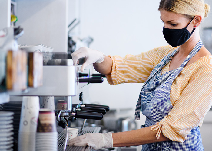 A woman wearing a mask and apron operates an espresso machine