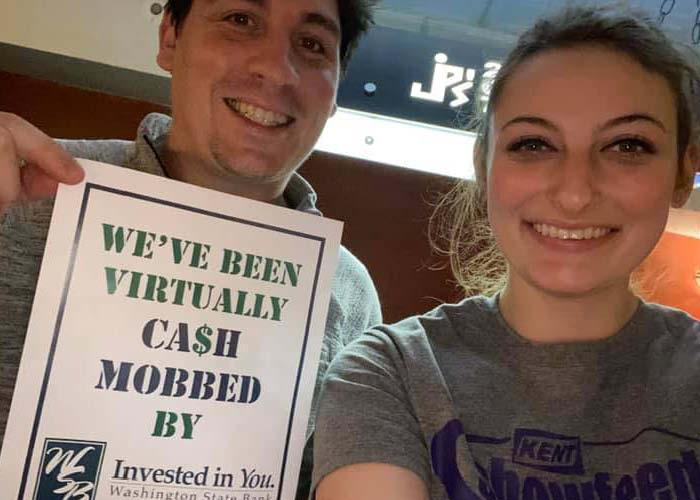 Two people hold up a sign that got them $15 off a meal at a local restaurant
